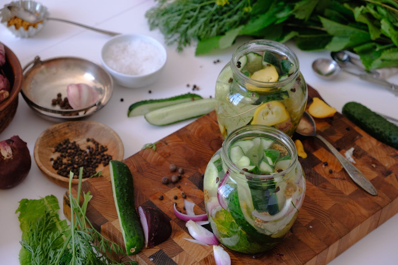 High angle view of glass jars filled with homemade pickles on a wooden board with herbs and spices.